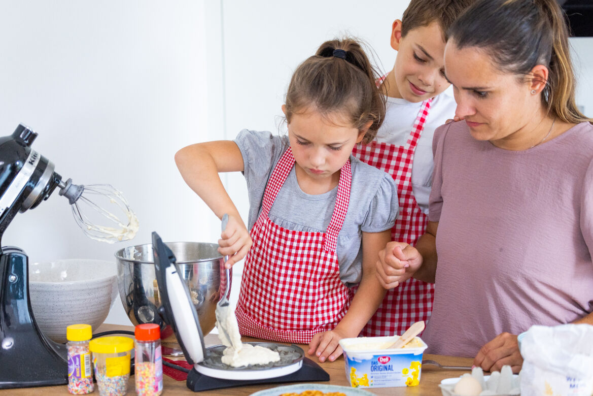 Eine Frau bereitet gemeinsam mit ihren Kindern Waffeln zu.